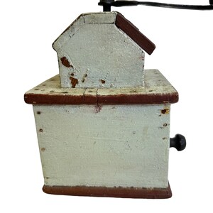 May include: A vintage wooden coffee grinder with a hand crank. The grinder is painted white with red accents and has a small drawer on the side.