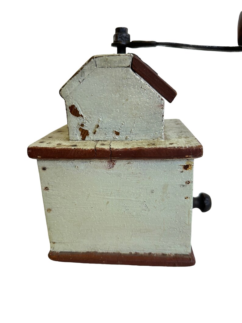 May include: A vintage wooden coffee grinder with a hand crank. The grinder is painted white with red accents and has a small drawer on the side.