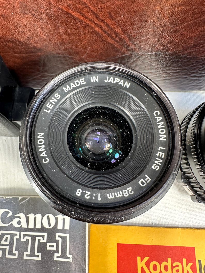 May include: A black Canon FD 28mm 1:2.8 lens with the text "LENS MADE IN JAPAN CANON LENS FD 28mm 1:2.8" printed on the side.