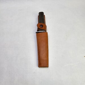 May include: A brown leather sheath with a snap closure, holding a black handled knife.