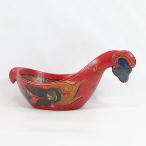 Könnte beinhalten: Eine rote Holzschale mit einem Ziegenkopf als Griff. Die Schale ist mit traditionellen schwedischen Volkskunstmotiven in Gelb, Blau und Grün bemalt.