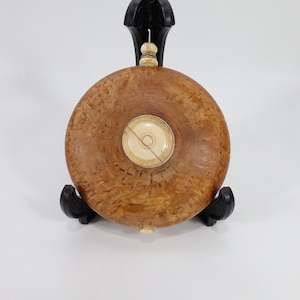 May include: A round wooden flask with a decorative ivory inlay. The flask is brown with a wood grain pattern and is sitting on a black stand.