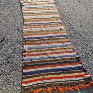 May include: A long, narrow, striped rug with orange fringe. The rug has a variety of colors, including red, orange, yellow, green, blue, and brown.