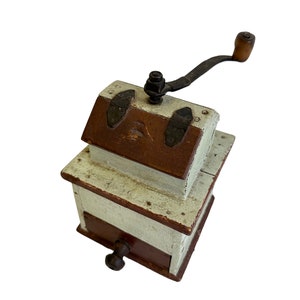 May include: A vintage wooden coffee grinder with a hand crank and a drawer. The grinder is painted white with brown accents and has metal accents.