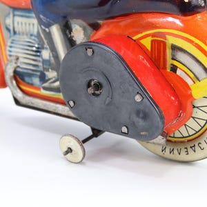 May include: Vintage toy motorcycle in red, orange, yellow, and blue. The motorcycle has a black side panel and a white tire with text. The toy has a small white wheel for balance.