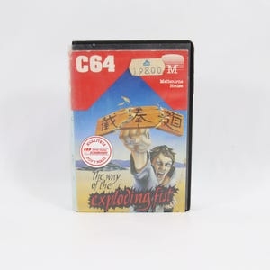 Könnte beinhalten: Eine Vintage C64-Spielkassette mit rotem und blauem Cover. Das Cover zeigt einen Mann, der ein Holzbrett zerbricht, mit dem Titel "The way of the exploding fist".