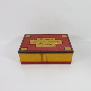 May include: A vintage yellow and red rectangular tin box with black lettering that reads "Tönsberg Margarinfabrik Tönsberg".