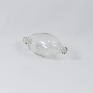 May include: A clear glass object shaped like a long, thin oval with rounded ends. The object is lying on a white surface.