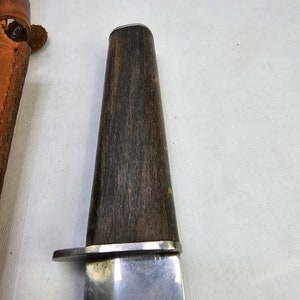 May include: A close-up of a silver knife with a dark wood handle. The knife has a rounded tip and a slightly curved blade.