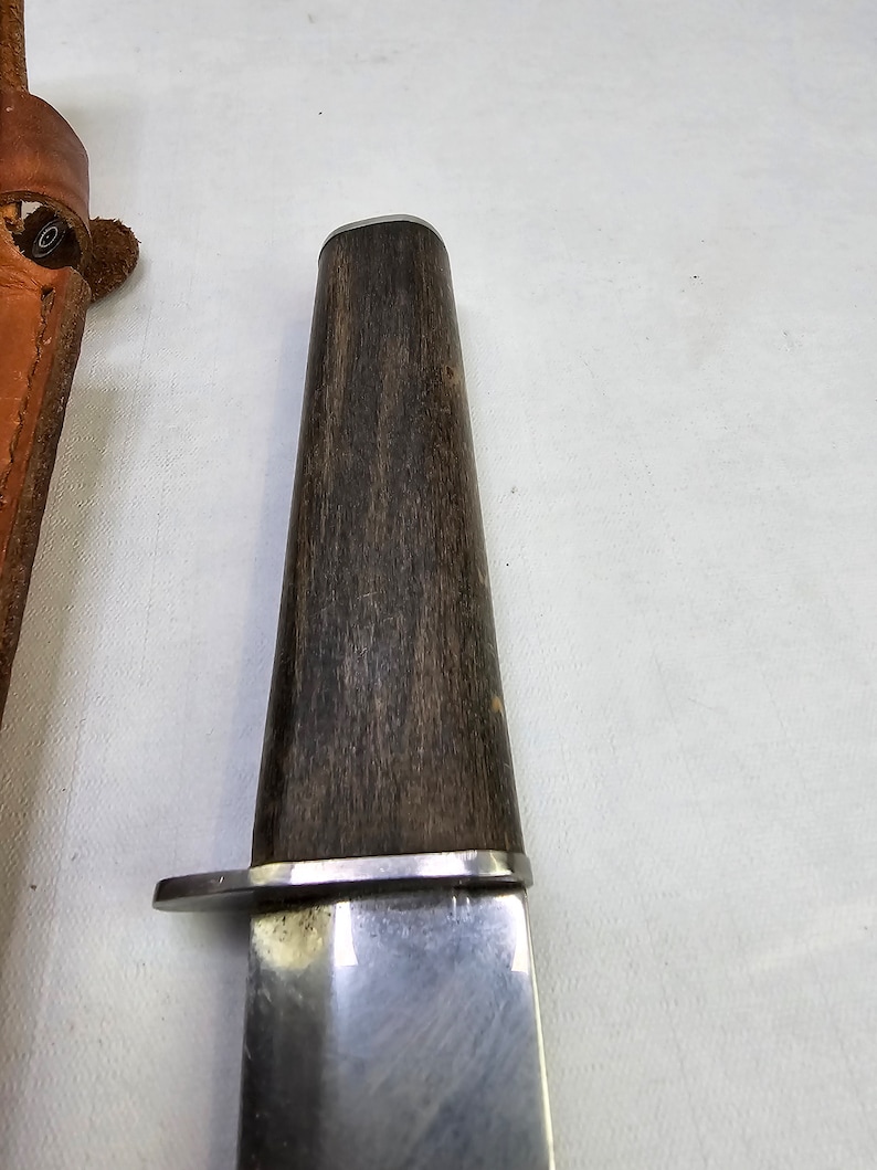 May include: A close-up of a silver knife with a dark wood handle. The knife has a rounded tip and a slightly curved blade.