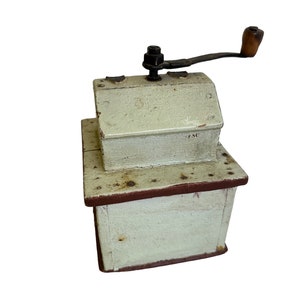 May include: A vintage wooden coffee grinder with a hand crank. The grinder is painted white with red accents and has a small metal plate with the number "75C" on it.