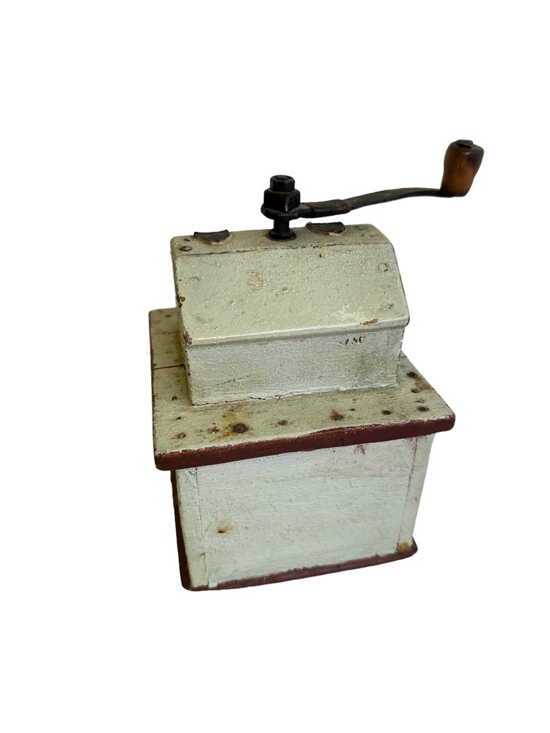 May include: A vintage wooden coffee grinder with a hand crank. The grinder is painted white with red accents and has a small metal plate with the number "75C" on it.