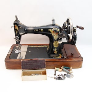 May include: Vintage Singer sewing machine, black with gold floral detailing, on a wooden base. Includes a small wooden box with sewing accessories and spools of thread. A classic sewing tool.