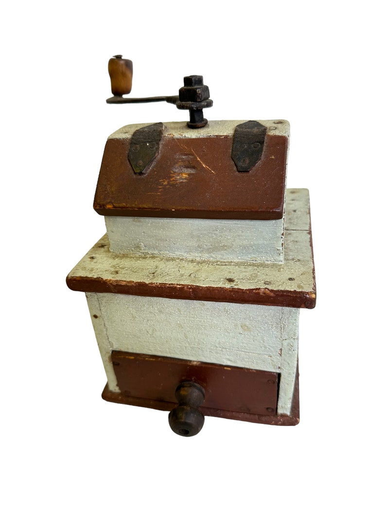 May include: Antique wooden coffee grinder with a hand crank, painted white with brown accents. The grinder has a drawer for collecting coffee grounds.