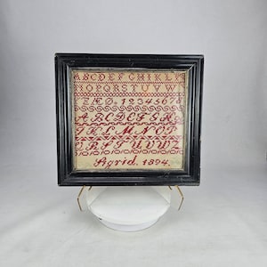 May include: A framed sampler with red embroidered letters of the alphabet, numbers, and the date "Agrid. 1894."