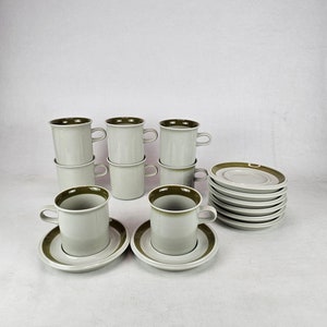 Puede incluir: Juego de seis tazas de café de cerámica blanca con una banda verde alrededor de la parte superior. Las tazas están apiladas en pares. También hay seis platillos a juego con una banda verde alrededor del borde.
