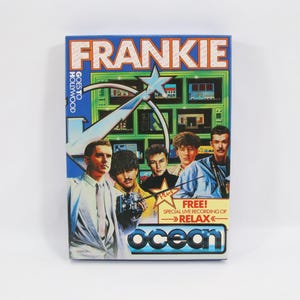 Puede incluir: Una caja de videojuego vintage de "Frankie Goes to Hollywood". La caja es azul con el nombre de la banda en blanco y un gráfico de estrella. La portada presenta imágenes de los miembros de la banda y el logotipo de Ocean.
