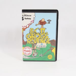 Puede incluir: Un cartucho de videojuego negro con el título "B.C. II, Grog's Revenge". El cartucho tiene una colorida ilustración de personajes de dibujos animados en un entorno prehistórico. El texto "Sydney" también es visible.