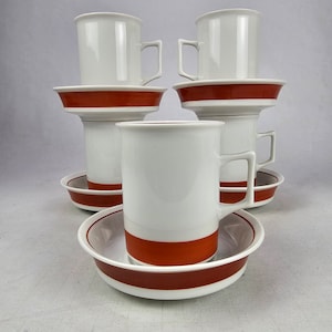 Puede incluir: Juego de seis tazas de café de cerámica blanca con bandas naranjas alrededor de la parte superior de las tazas y los platillos.