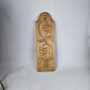 May include: A wooden wall hanging with a carved floral design. The design features two flowers with intricate details and leaves.