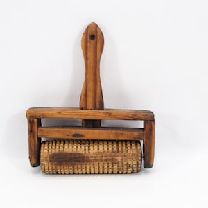 May include: A vintage wooden pastry docker with a handle and a textured roller. The handle is long and slender, and the roller is covered in small, evenly spaced points. The wood has a warm, natural tone.