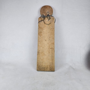 May include: A long, rectangular wooden cutting board with a round knob at the top. The board is tied with a black ribbon.