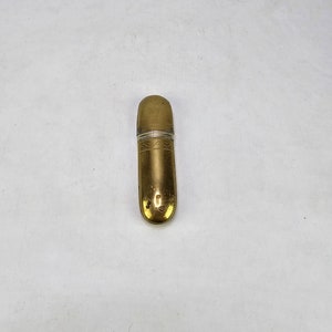 May include: A gold-colored metal container with a clear glass top. The container has a decorative design.
