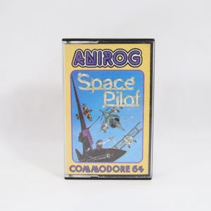 以下が含まれることがあります： Anirogの「Space Pilot」のビンテージCommodore 64ビデオゲームカートリッジ。ラベルは、宇宙船やその他の航空機の宇宙をテーマにしたイラストが描かれた青色の背景です。ゲームタイトルと会社名がはっきりと表示されています。