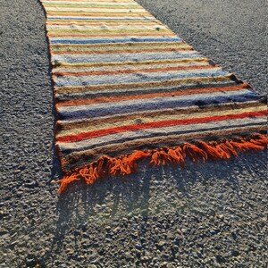 May include: A long, colorful striped rug with orange fringe. The rug is made of woven fabric and has a variety of colors, including red, orange, yellow, green, blue, and brown.