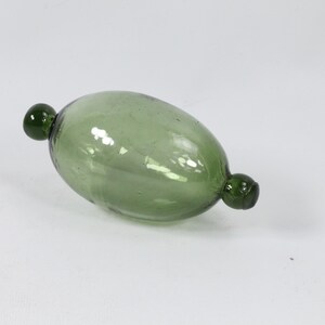 May include: A green glass bottle stopper with rounded ends. The bottle stopper is oval shaped and has a smooth, glossy finish.