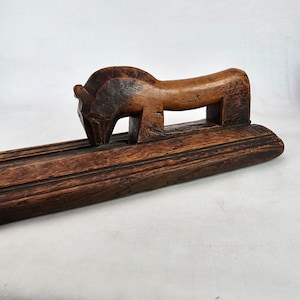 Pode incluir: Uma escultura de madeira de um animal estilizado, possivelmente um cavalo ou um touro, com um corpo longo e delgado e um pescoço curvo. A escultura é esculpida em um estilo simples e rústico e tem um acabamento marrom escuro. A escultura é montada em uma base de madeira.