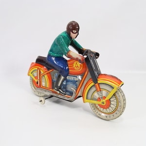 Vintage Soviet tin wind-up motorcycle toy made in USSR in the 1950s. Bright lithographed red, yellow, and green colors with a rider in green and blue. The wind-up mechanism is working though the key is not included. Shows wear and small scratches consistent with use. Measures about 21 cm long, 8 cm wide, and 15 cm high. A colorful and collectible mechanical tin toy from the Soviet era.