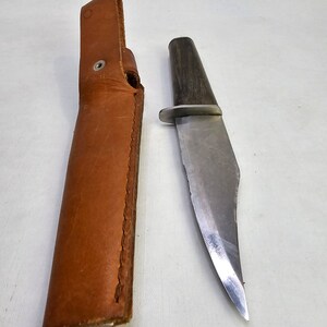 May include: A brown leather sheath with a silver snap and a silver blade knife with a dark wood handle.