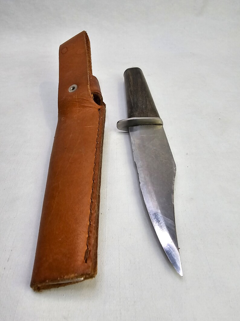 May include: A brown leather sheath with a silver snap and a silver blade knife with a dark wood handle.