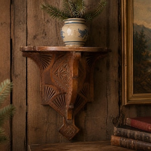 Peut inclure: Étagère en bois sculpté avec des motifs d'étoiles et d'éventails. Un petit pot en céramique bleu et blanc avec de la verdure est posé sur l'étagère. L'étagère est fixée à un mur en bois, avec un tableau encadré et des livres en arrière-plan.