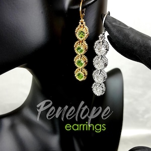 May include: Two pairs of dangle earrings. One pair is gold-toned with green gemstones, the other is silver-toned with clear gemstones. The earrings are displayed on a black mannequin head and hand. The text "Penelope earrings" is in the image.