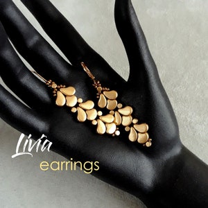 May include: Gold-toned earrings with a teardrop design. The earrings are made of small beads and are arranged in a cascading pattern. The earrings are labelled "Livia earrings".