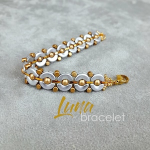 May include: A silver and gold bracelet with a repeating pattern of half circles. The bracelet has a clasp closure.