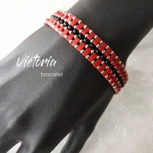 Könnte beinhalten: Ein rotes, schwarzes und silbernes Perlenarmband mit dem Text "Victoria bracelet" im Hintergrund.