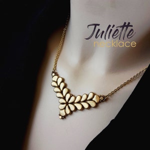 Op de afbeelding: Een gouden ketting met een uniek ontwerp met een reeks traanvormige kralen die in een V-vorm zijn gerangschikt. De ketting heet "Juliette necklace".