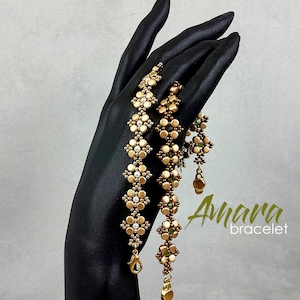 May include: Two gold and brown beaded bracelets with a white bead accent. The bracelets are stacked on a black mannequin hand. The text "Amara bracelet" is visible in the image.