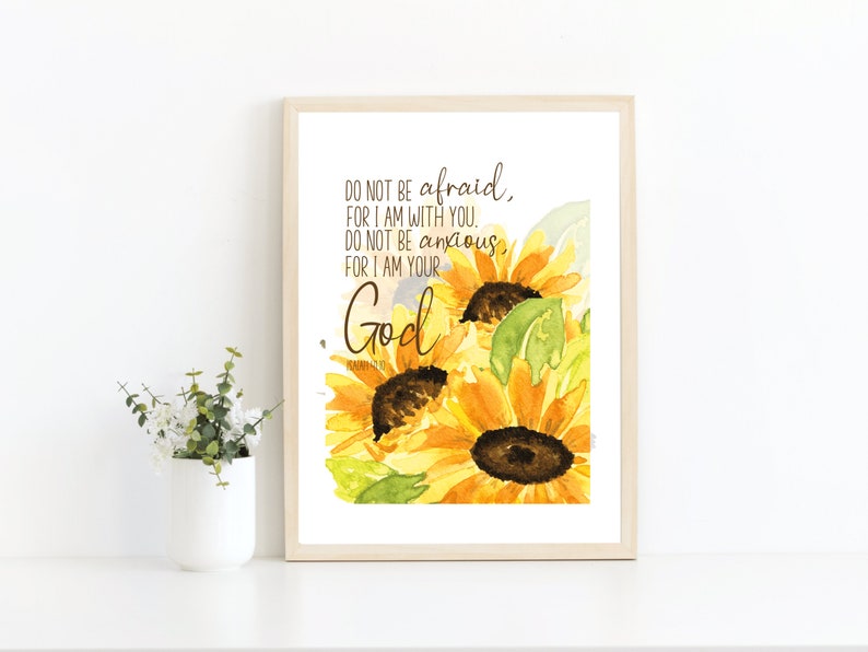 Op de afbeelding: Een aquarel van zonnebloemen met de tekst "DO NOT BE afraid, FOR I AM WITH YOU. DO NOT BE anxious, FOR I AM YOUR God" gedrukt op een witte achtergrond.