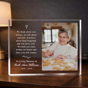 May include: A clear acrylic memorial plaque featuring a photograph and text. The text reads "In Loving Memory of Ruth Ann Williams 1940-2026" and a touching message. The photo shows an elderly woman smiling while baking.