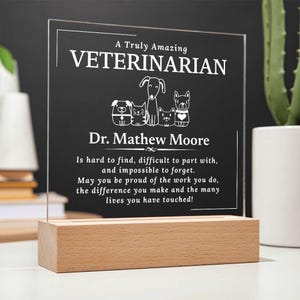May include: A white acrylic plaque with a wood base, illuminated from behind. The plaque reads "A Truly Amazing Veterinarian" with a line of cartoon animals and the text "Dr. Mathew Moore". The plaque continues with the text "Is hard to find, difficult to part with, and impossible to forget. May you be proud of the work you do, the difference you make and the many lives you have touched!"