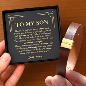 Peut inclure: Un bracelet en cuir marron avec un fermoir doré orné d'un motif de vague. Le bracelet est présenté à côté d'une boîte noire avec le texte "TO MY SON" et un message de "Love, Mom".