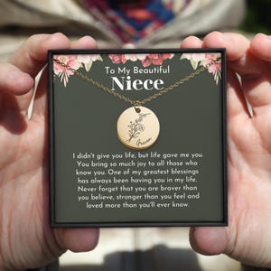 May include: A gold necklace with a round pendant featuring a floral design and the name "Fracen" engraved on it. The necklace is in a black box with a floral design and the text "To My Beautiful Niece".
