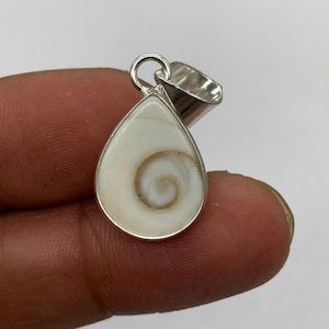 May include: A teardrop-shaped pendant featuring a white Shiva eye shell with a natural brown spiral pattern, encased in a polished silver-toned metal setting with a circular bail at the top for attachment to a necklace chain or cord.