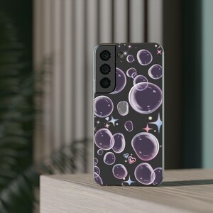 Puede incluir: Una funda negra para smartphone con un patrón de burbujas moradas, estrellas y corazones. Las burbujas varían en tamaño y transparencia, creando un diseño caprichoso. La funda tiene un recorte para la cámara y botones.