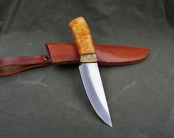 May include: A handmade knife featuring a light-coloured wooden handle and a polished steel blade. The knife is placed on a brown leather sheath, with a matching leather belt loop. The blade has the initials "HO" etched near the handle.