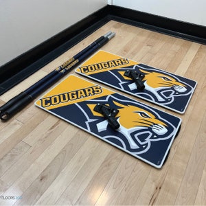 May include: Two blue and yellow floor signs with the word "Cougar" and a graphic of a cougar. The signs are on a wooden floor with two long blue and yellow cleaning poles.